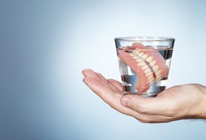 Outstretched hand holding glass of water with dentures in Wharton 