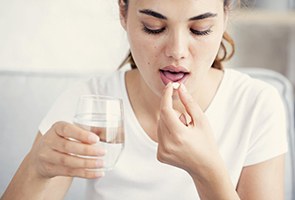 young woman taking pill with glass of water 