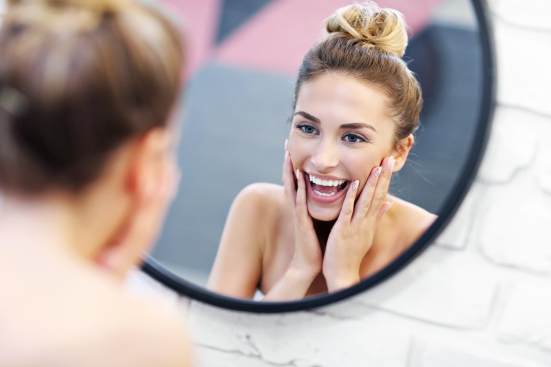 Person with beautiful smile from emergency dentist in Wharton looking in mirror 
