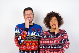 Man and woman wearing seasonal sweaters and holding one side of their mouths in pain